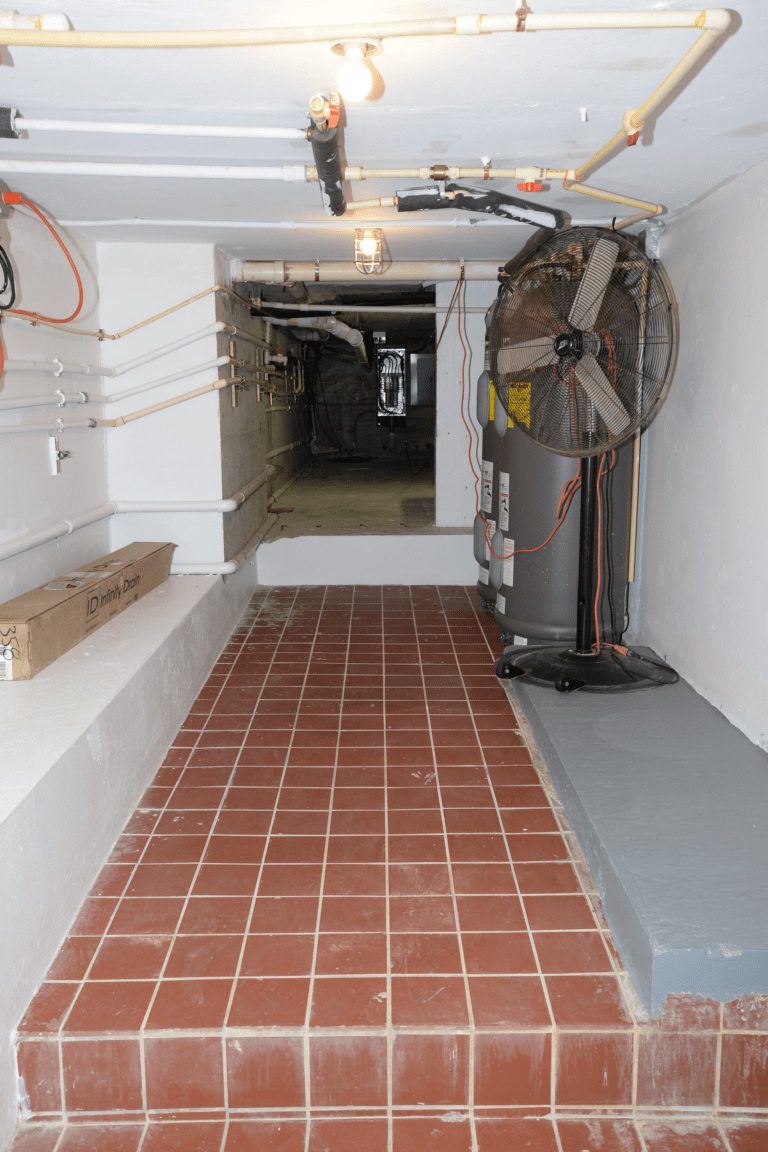 A basement hallway with exposed water pipes and a large water heater
