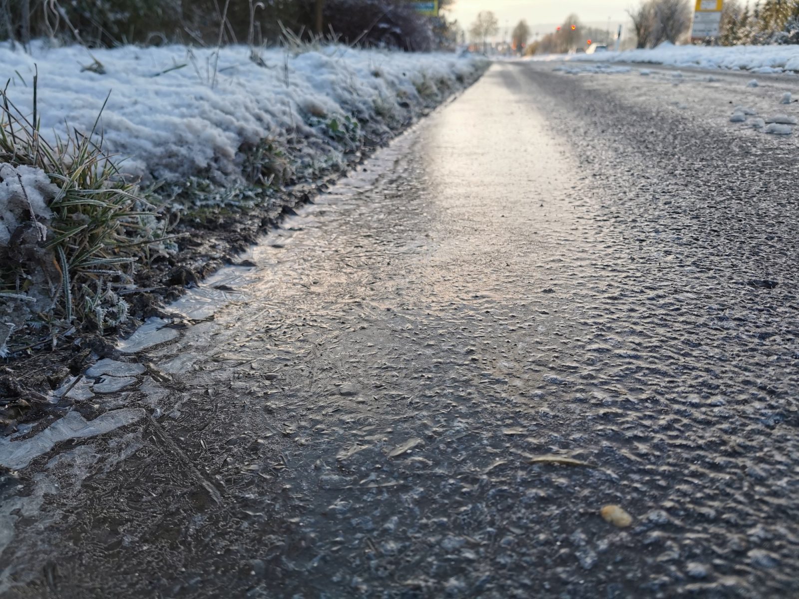 A road surface coated with a thin, glossy, nearly transparent sheet of black ice, with snow piled at the roadside in Tauberbischofsheim, Germany